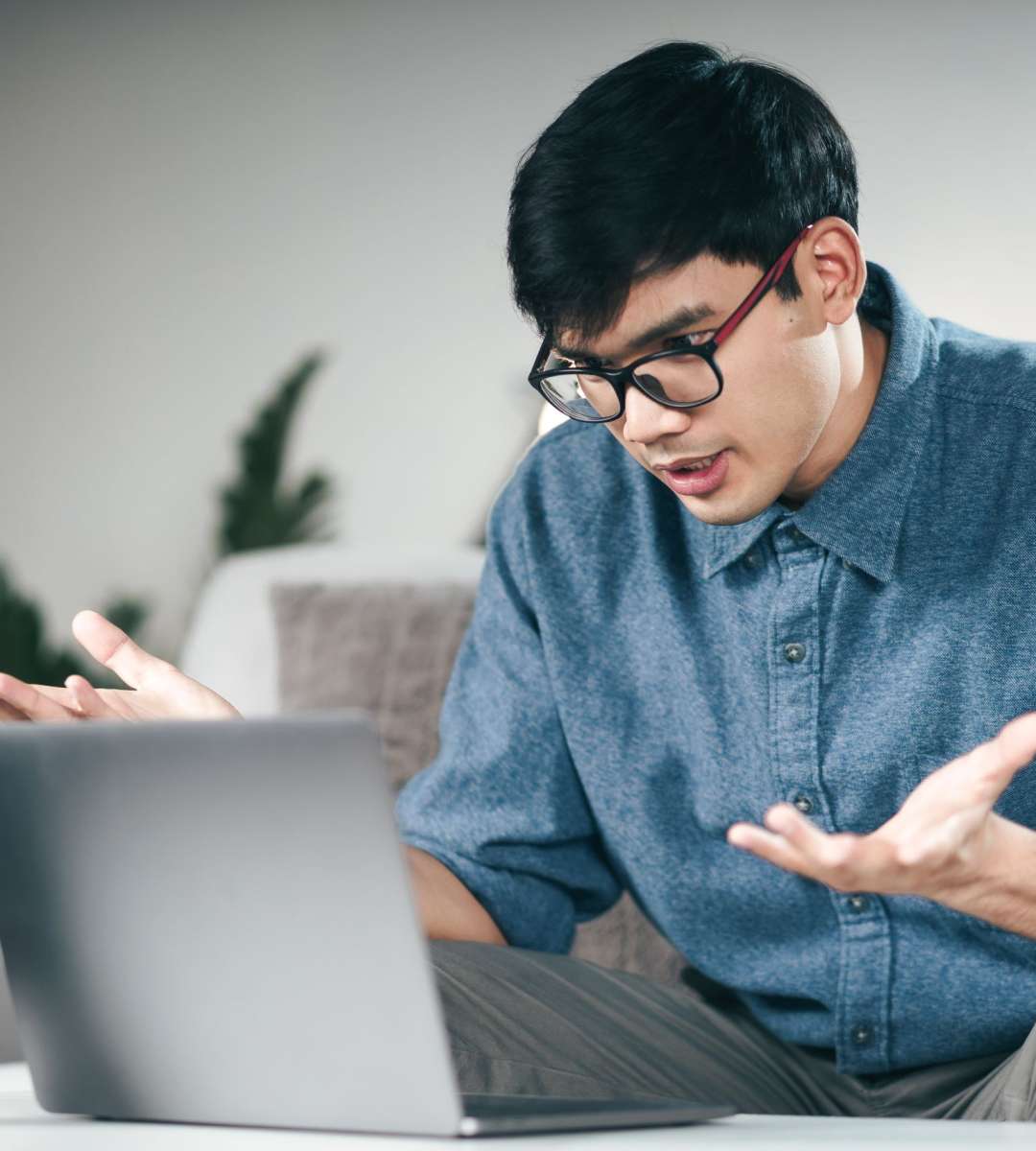 Young Asian man using laptop for online video conference call seriously explain talking on the couch in living room at night.