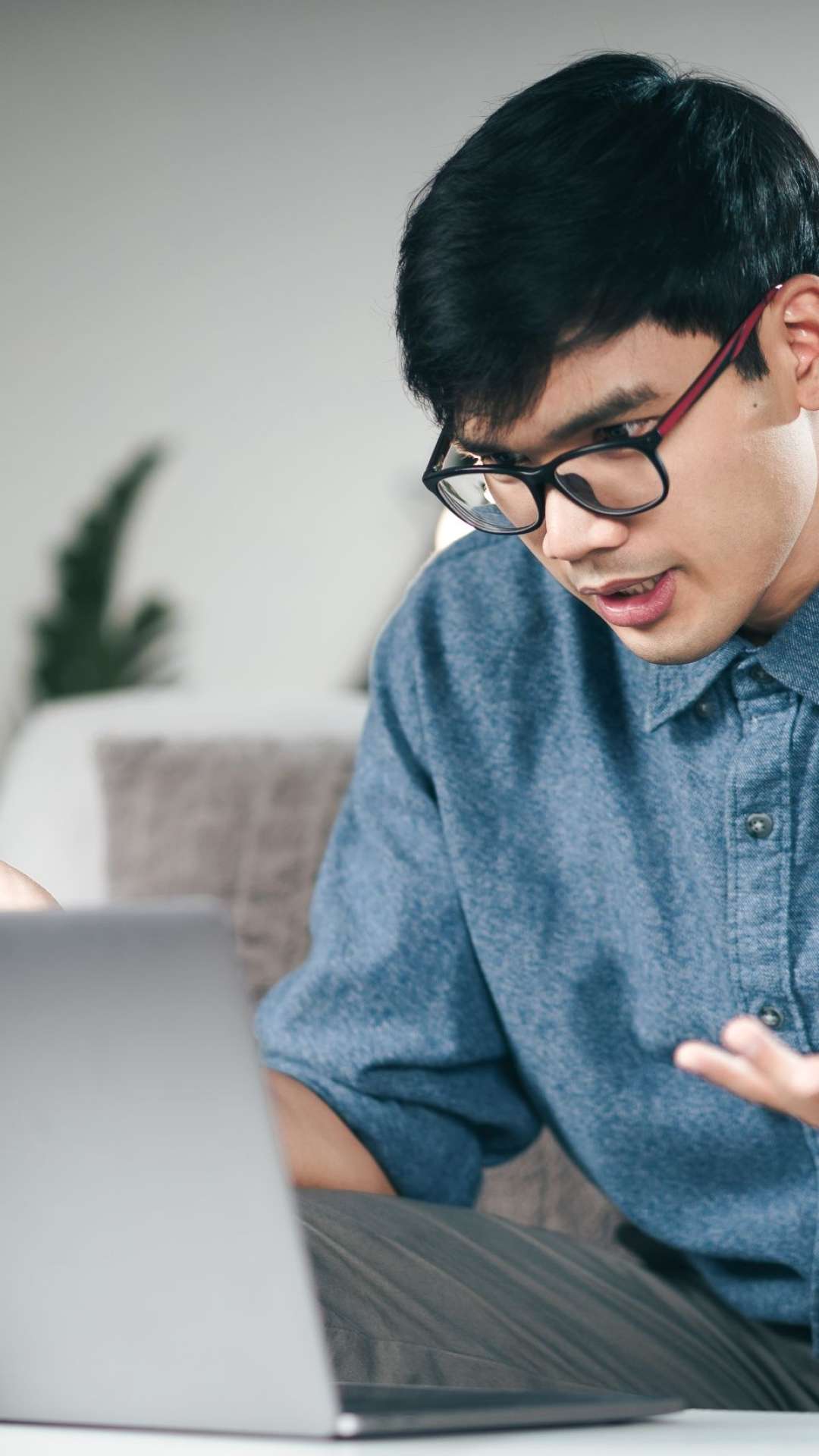 Young Asian man using laptop for online video conference call seriously explain talking on the couch in living room at night.